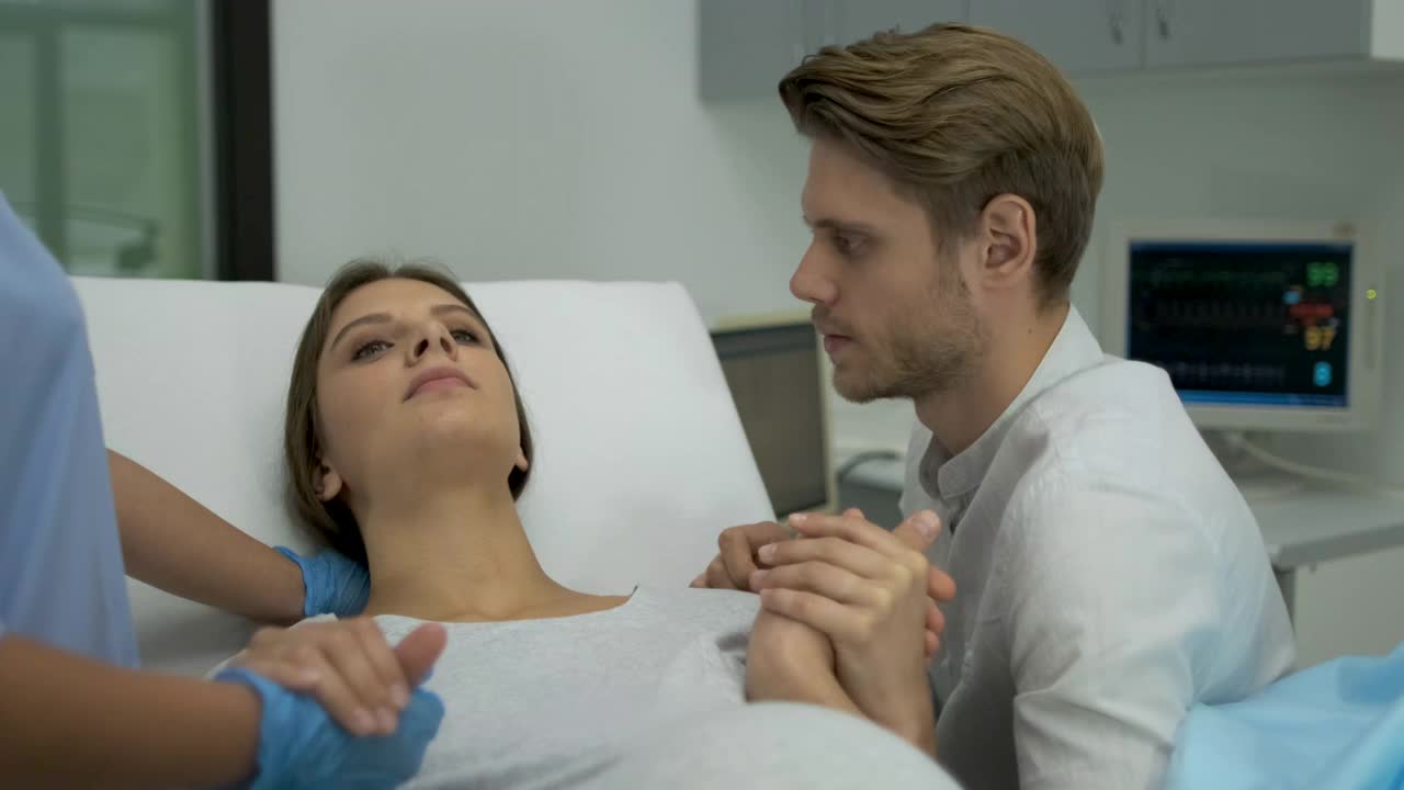 分娩，妇产医院，分娩。医院急诊:妇女分娩，丈夫握着她的手支持，产科医生助产。母亲，分娩的母亲，4 K慢动作