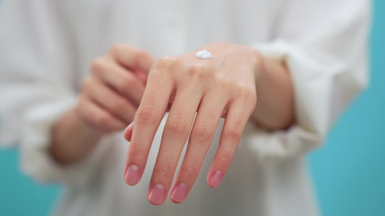 特寫(xiě)婦女的手和使用潤(rùn)膚霜，身體乳液，隔離在藍(lán)色背景。