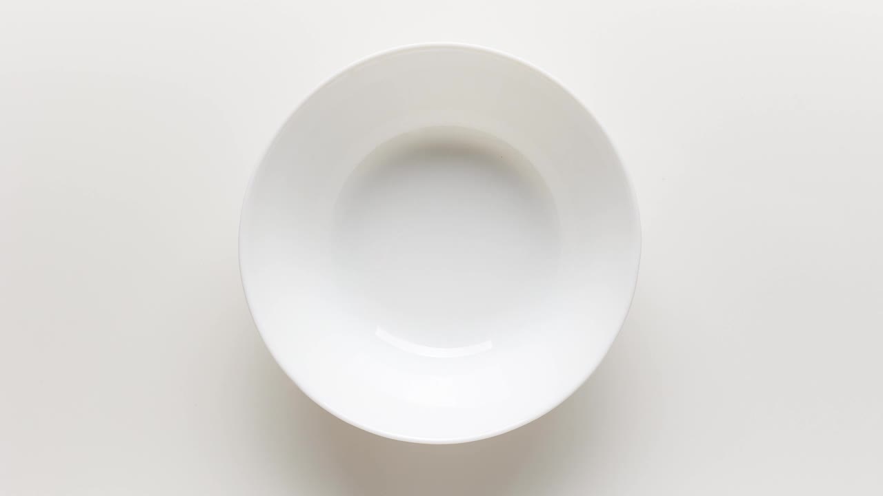 旋转碗的新鲜天然希腊酸奶装饰莓果和麦片在白色的背景，俯视图。定格动画