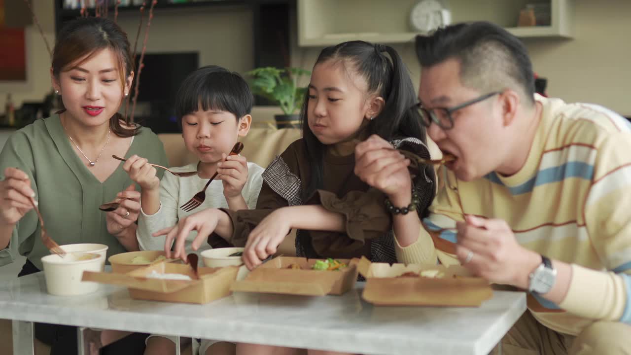 亚洲华人年轻家庭周末在客厅的电视前享受外卖食物