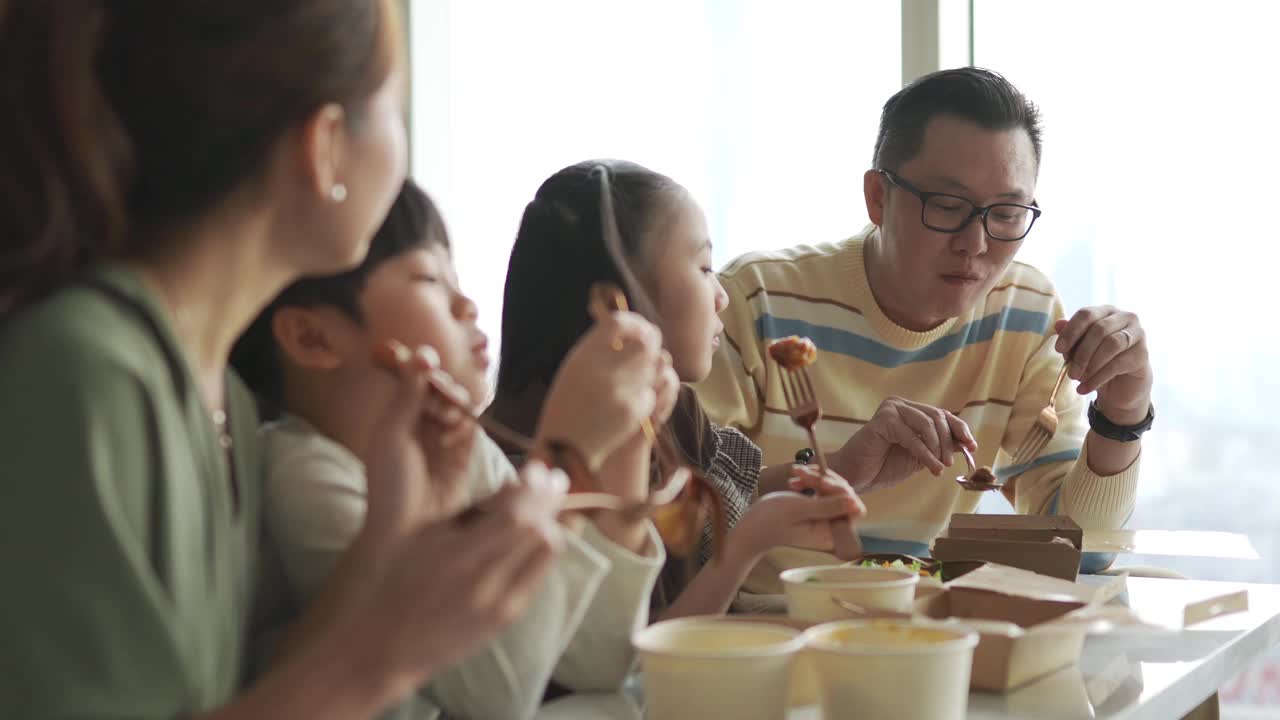 亚洲华人年轻家庭周末在客厅的电视前享受外卖食物