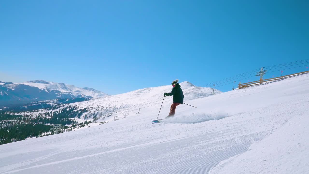 在远处有山的黑色菱形滑雪斜坡上跟踪或跟踪一个女滑雪运动员