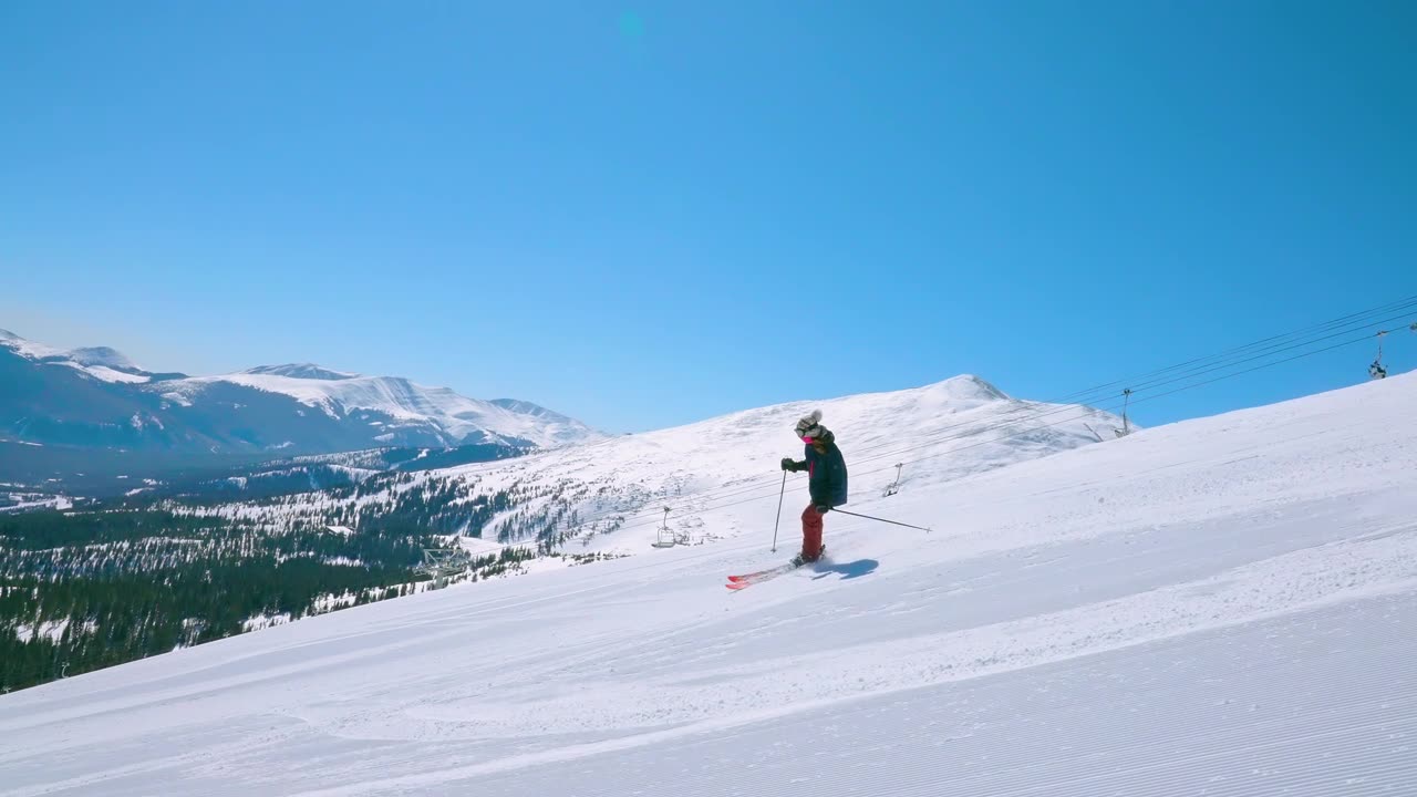 详情图-在远处有山的黑色菱形滑雪斜坡上跟踪或跟踪一个女滑雪运动员