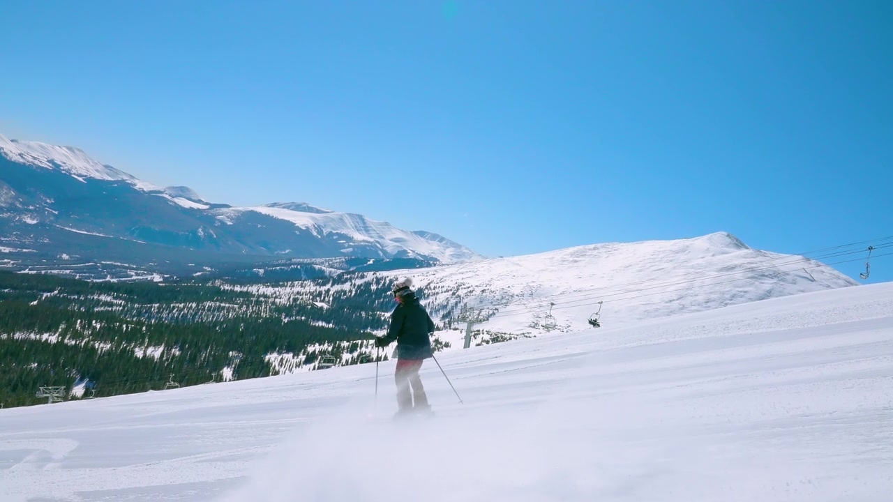 详情图-在远处有山的黑色菱形滑雪斜坡上跟踪或跟踪一个女滑雪运动员