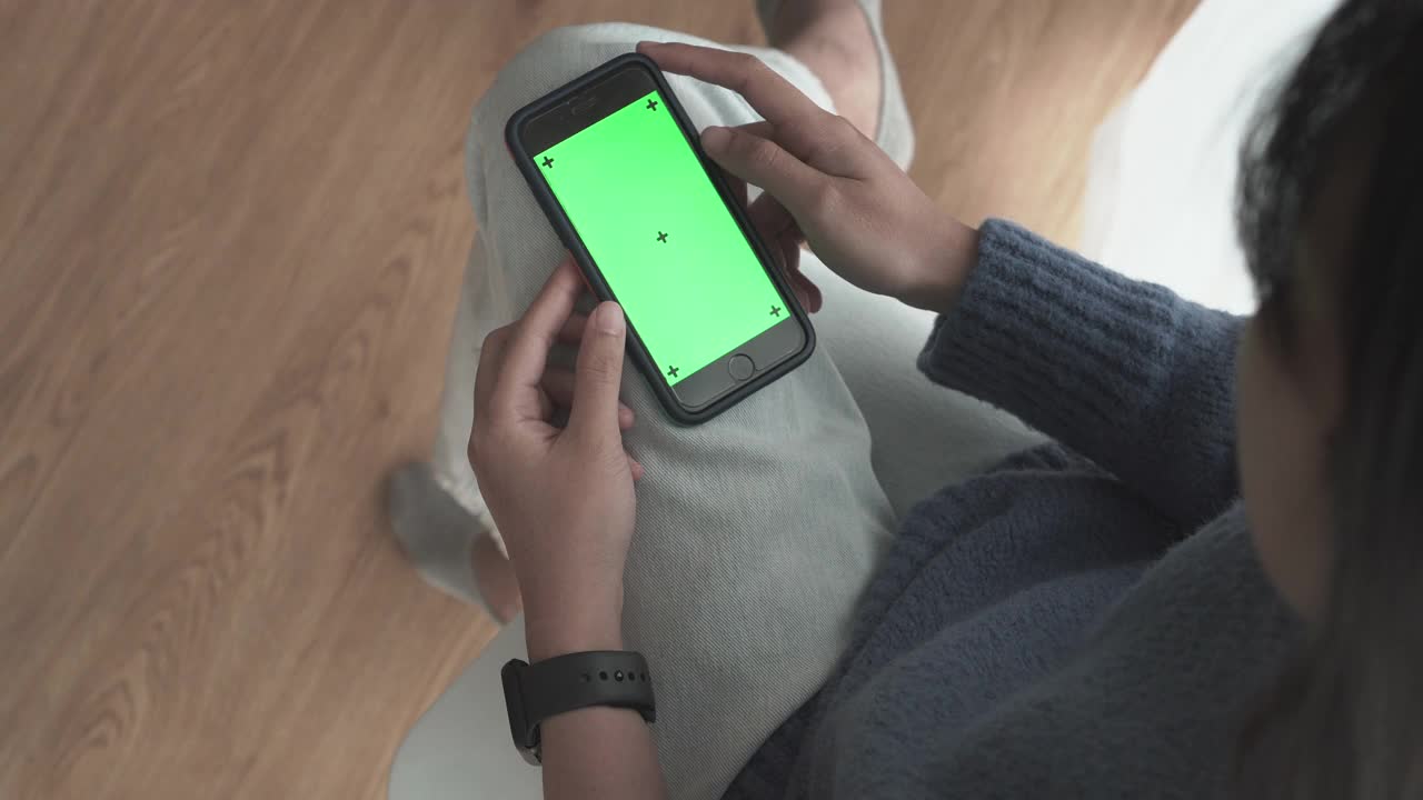 过肩拍摄的女人使用绿色屏幕智能手机和智能手表