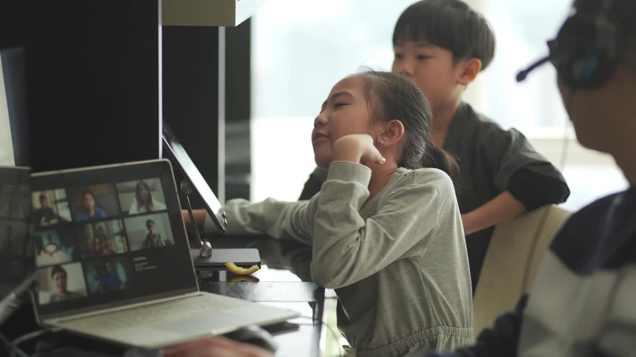 Lifehack亚洲华人父亲在家工作，用耳机与同事视频通话，而他的孩子在他旁边使用数字平板电脑