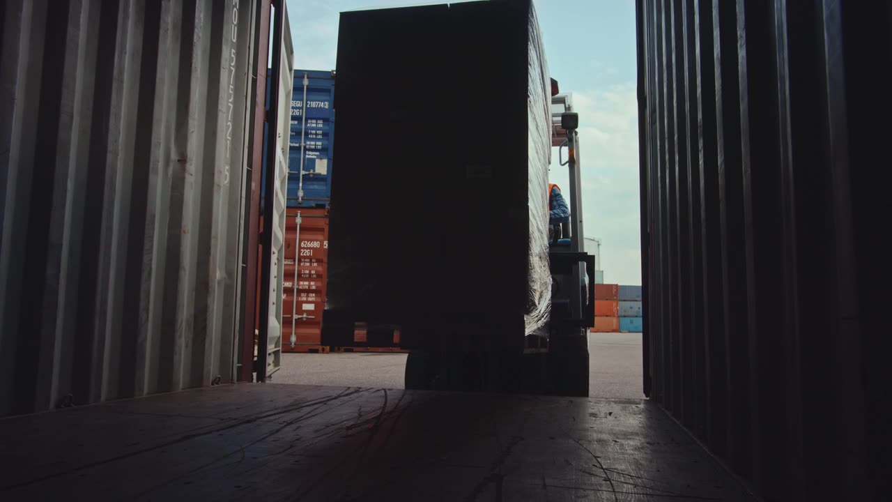 詳情圖-在物流作業(yè)港口碼頭，叉車司機(jī)用紙箱全托盤卸貨集裝箱。從內(nèi)部的相機(jī)視圖顯示托盤是如何提升和帶走。