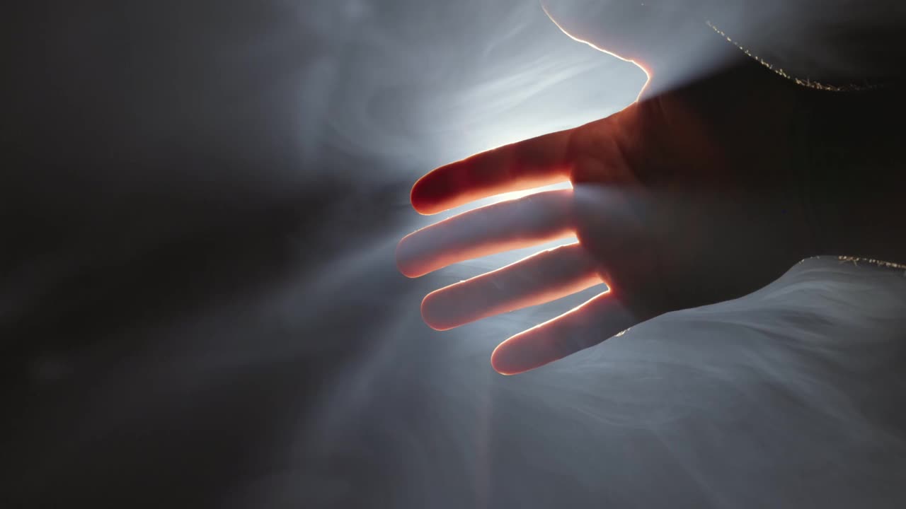 在接受帮助、支持和保护时，女性伸出手去触摸男性的手。给予帮助，希望和支持彼此的概念。背光，光线穿透手指和轻烟