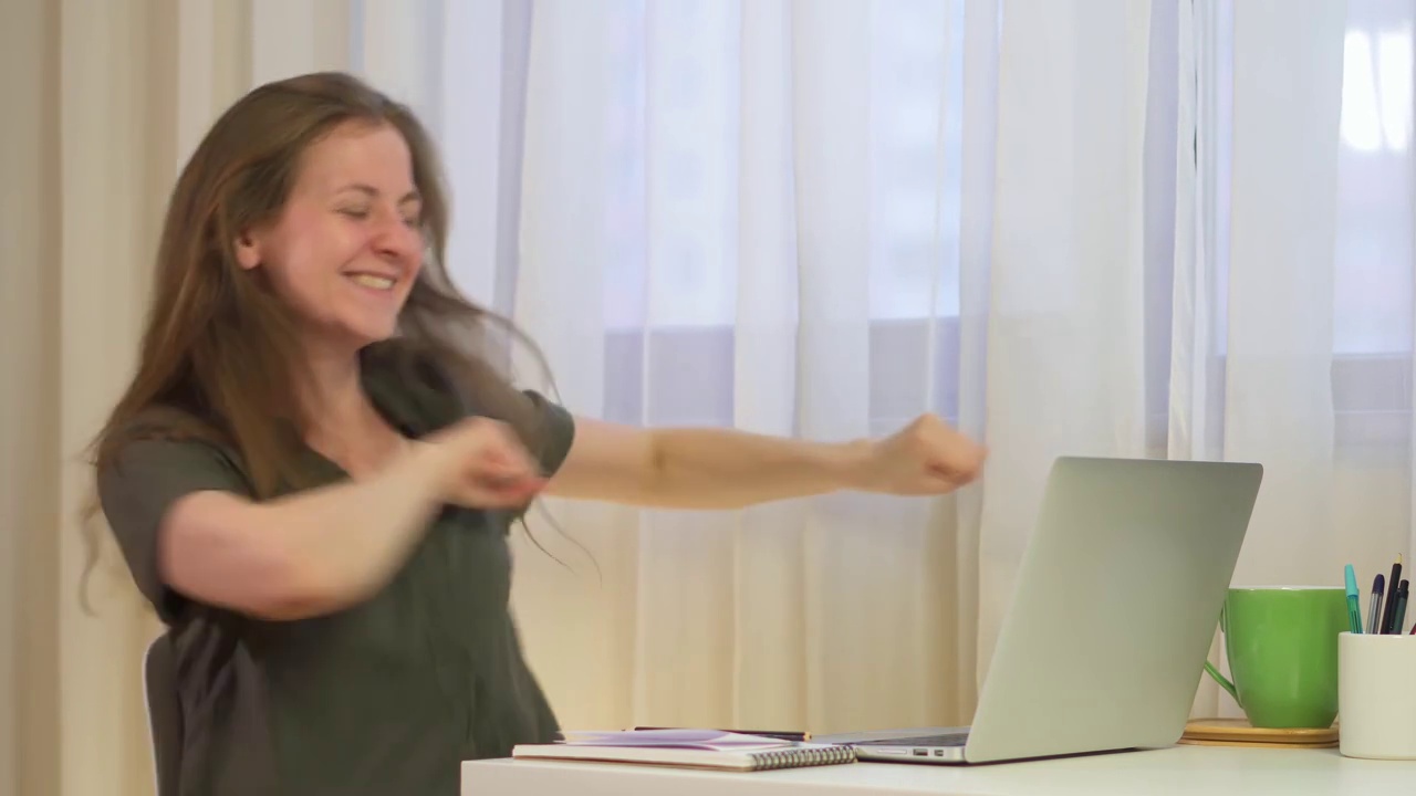 详情图-在笔记本电脑前欢舞庆祝胜利。一个妇女工作在家办公室很高兴。坐在电脑前的时候。知道好消息，喜欢在线交流。成人女孩有趣的笑话和戏剧。