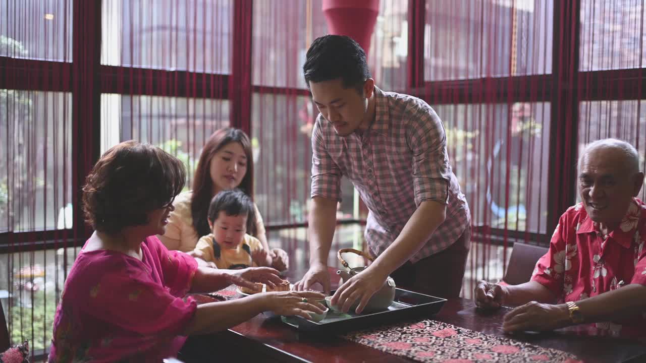 中国父亲在多代同堂期间奉上中国茶，在下午茶聚会期间享用传统的中秋节月饼和中国茶