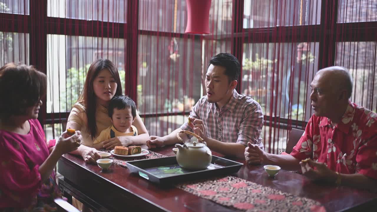 中国父亲与儿子在多代同堂期间享受传统的中秋节月饼和中国茶在家里下午茶聚会