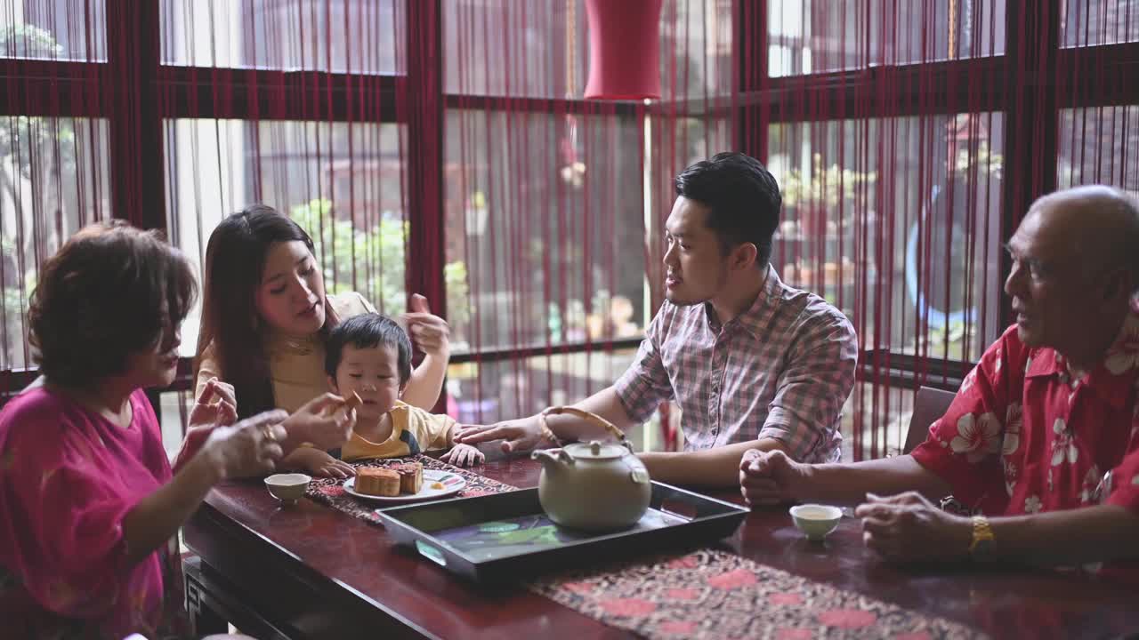 中国母亲喂养儿子在多代人享受传统中秋节月饼和中国茶在家里下午茶聚会