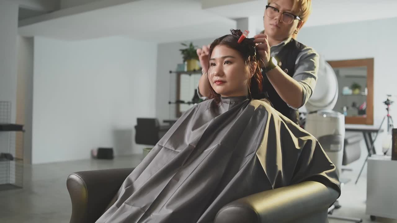 慢动作美发沙龙亚洲华裔女性发型师在美发沙龙为她的顾客剪发梳理湿长发