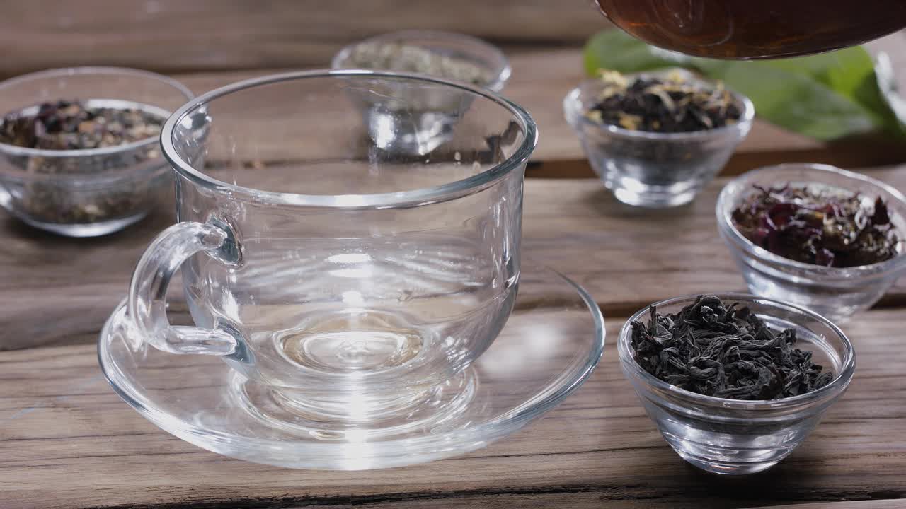 滴慢慢地掉进一杯茶。周围有小碗装着不同类型的茶叶。古董木制的桌子。