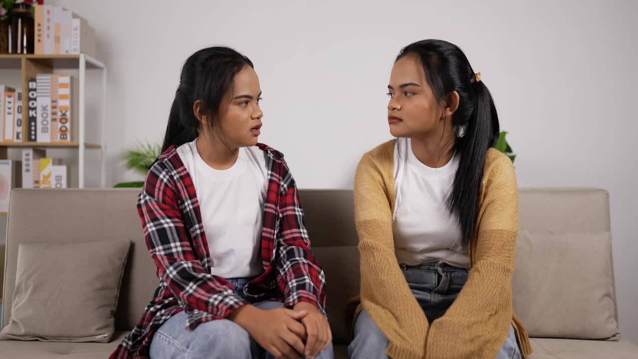亚洲双胞胎女孩坐在沙发上聊天