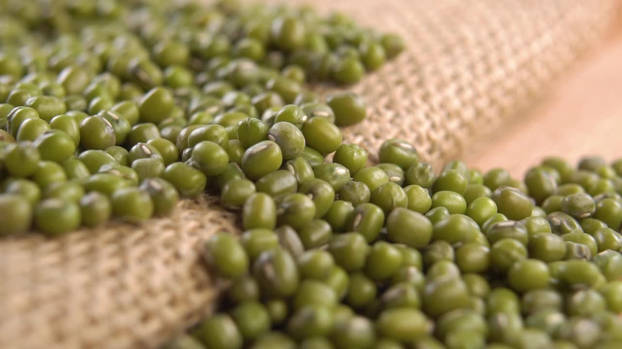 绿色的、干燥的、生的豆科植物以慢动作落在粗布上。绿豆