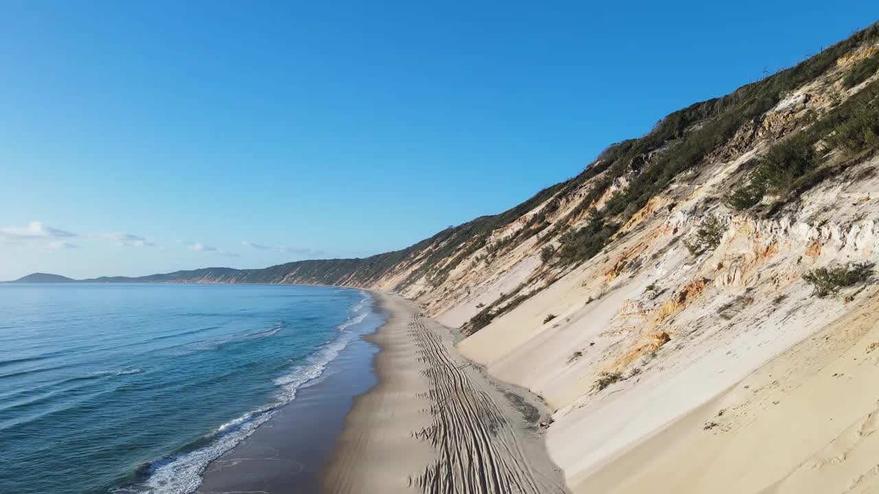 警车行驶在海浪和陡峭的沙崖之间，在废弃的海岸线海滩路上。