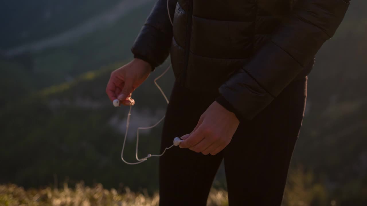 愉悦的女徒步者站在山顶俯瞰山谷，戴上耳机