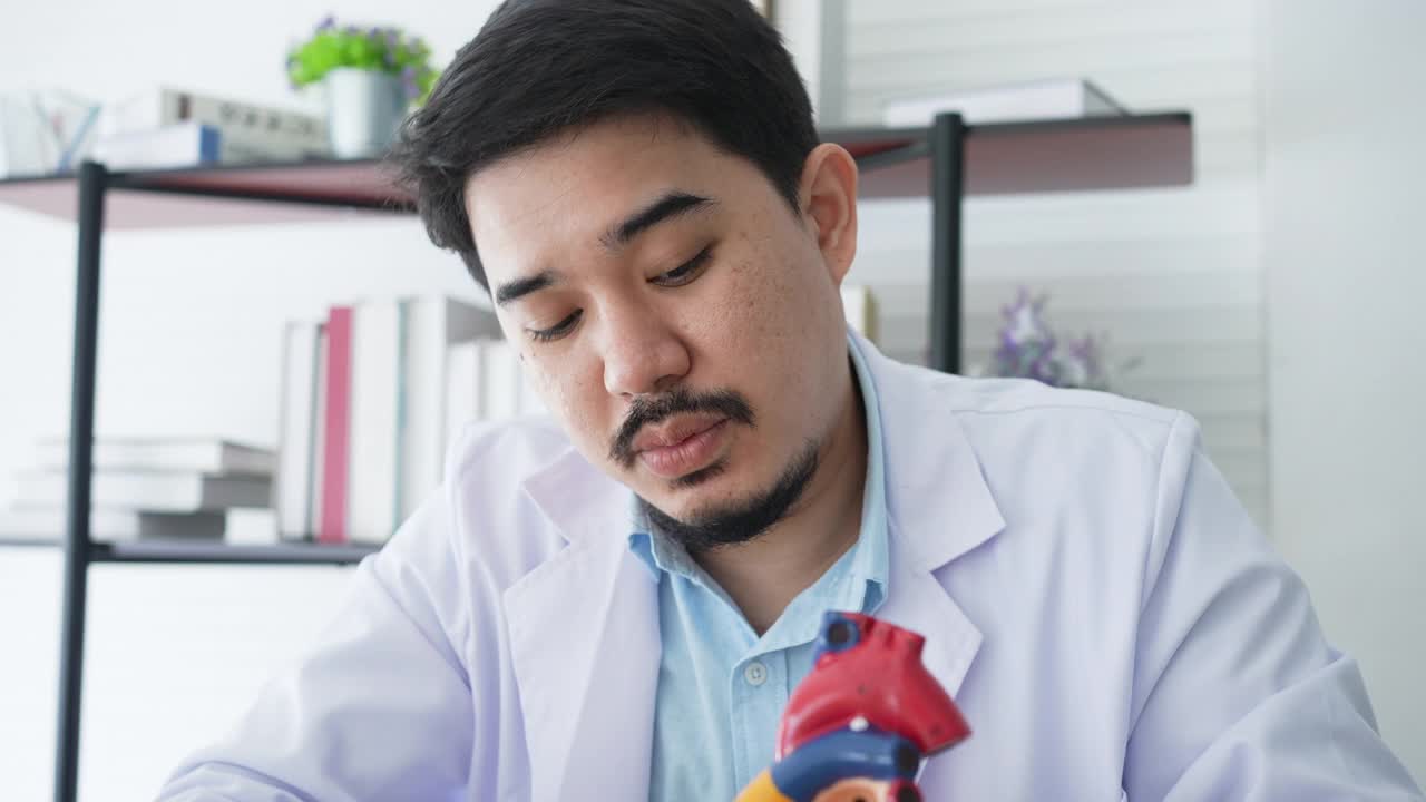慢动作心脏病专家专家指着心脏模型，通过远程医疗计划的健康和技术生活方式概念，给病人关于治疗心脏病发作的建议和咨询