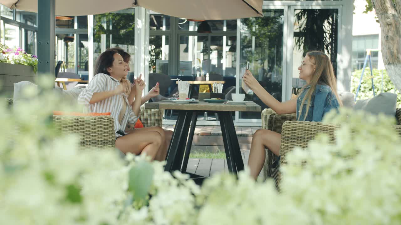 无忧无虑的女人在户外咖啡馆跳舞，而女性朋友在录像和大笑