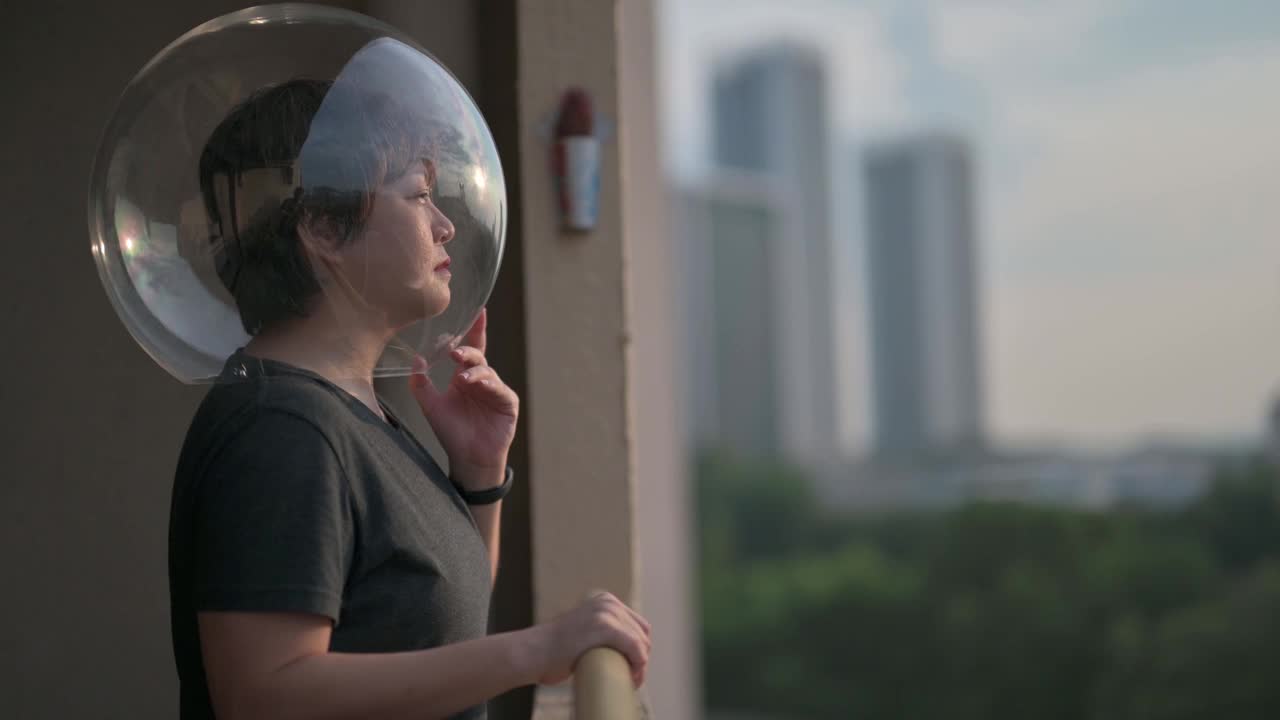 创意肖像侧视亚洲华人中成年妇女与透明的全头盔看从阳台