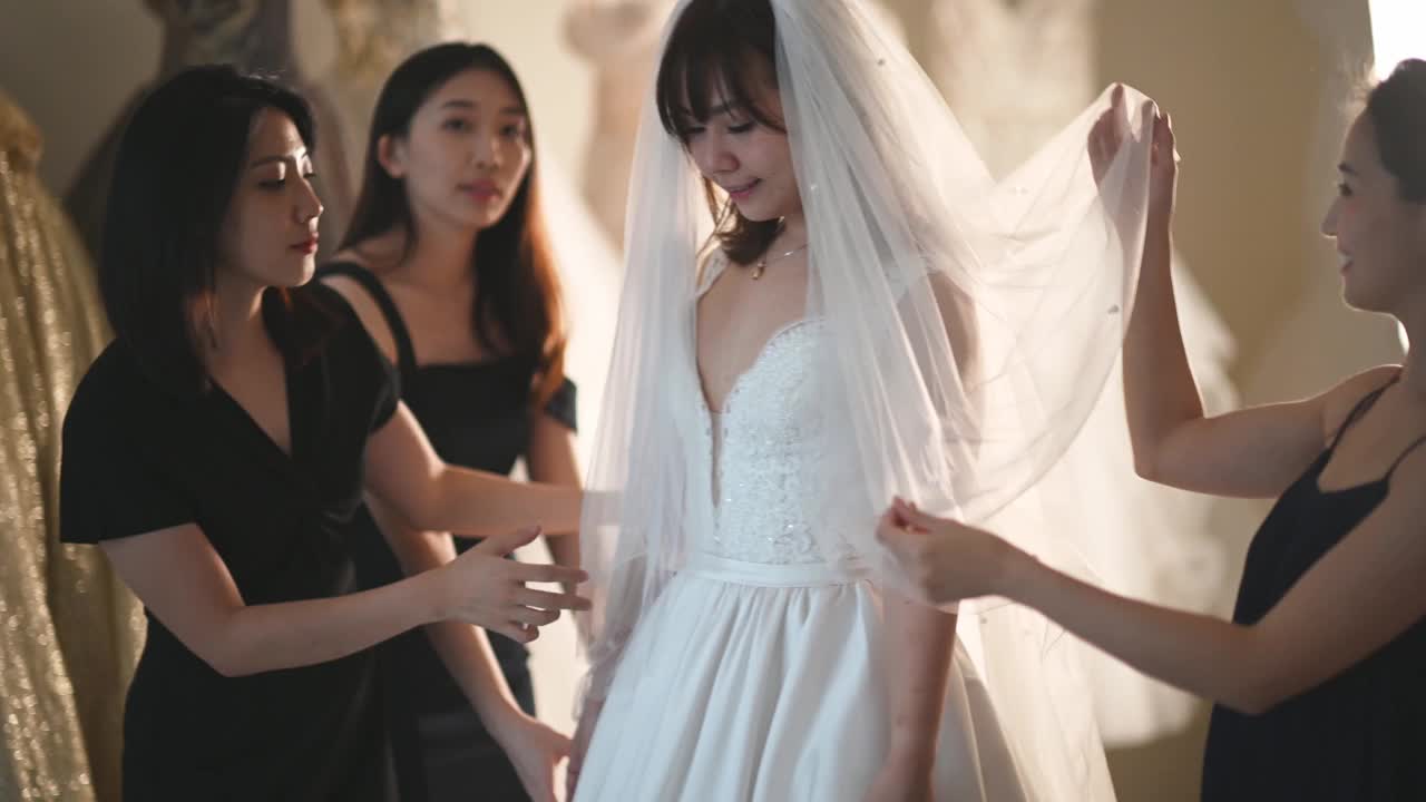 亚洲的中国新娘在婚纱店试穿婚纱，伴娘在旁边欣赏婚纱的美丽