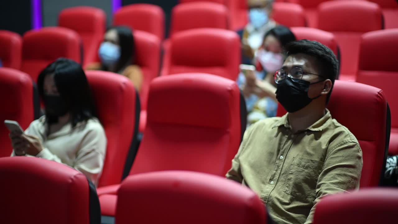 亚洲华人混合年龄段的人坐在电影院用智能手机等待电影放映时间