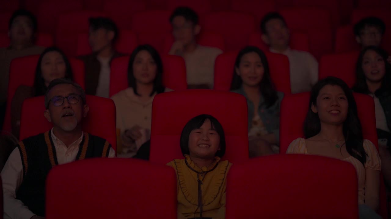 一位活跃的亚洲华人老人和他的孙女笑着在电影院看电影