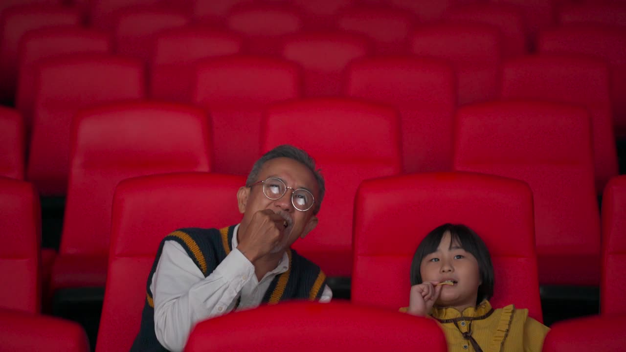 一位活跃的亚洲华人老人和他的孙女喜欢在电影院看电影