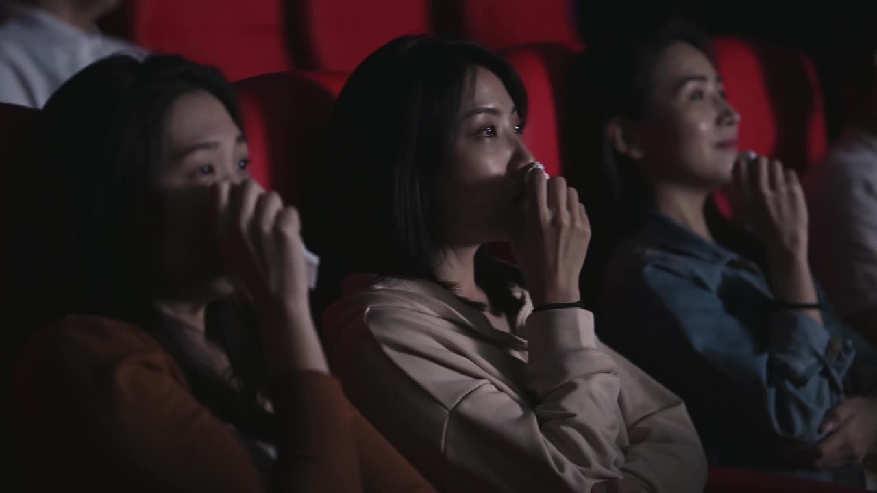 亚洲的中国女人在电影院看感伤的电影，在电影院用纸巾擦眼泪