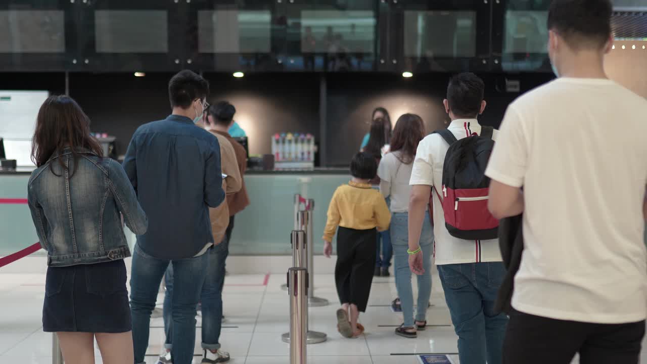 后视图亚洲人群，人们在电影院排队买电影票和小吃电影院与新常态的概念。社会距离。