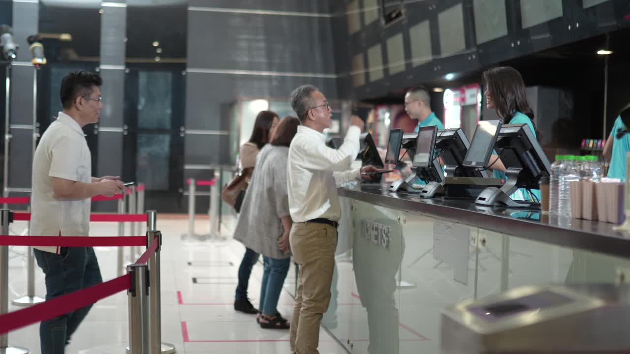 侧视亚洲人群，人们在电影院排队买电影票和快餐
