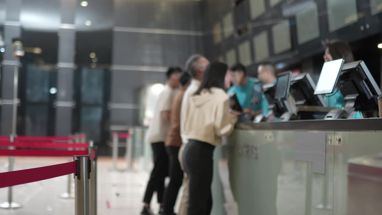 在电影院，一对亚洲华人父女在售票柜台前排队，用非接触式付款方式购买电影票