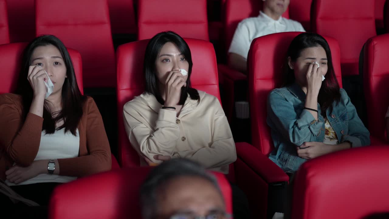亚洲的中国女性朋友在电影院看感伤的电影，在电影院用纸巾擦眼泪