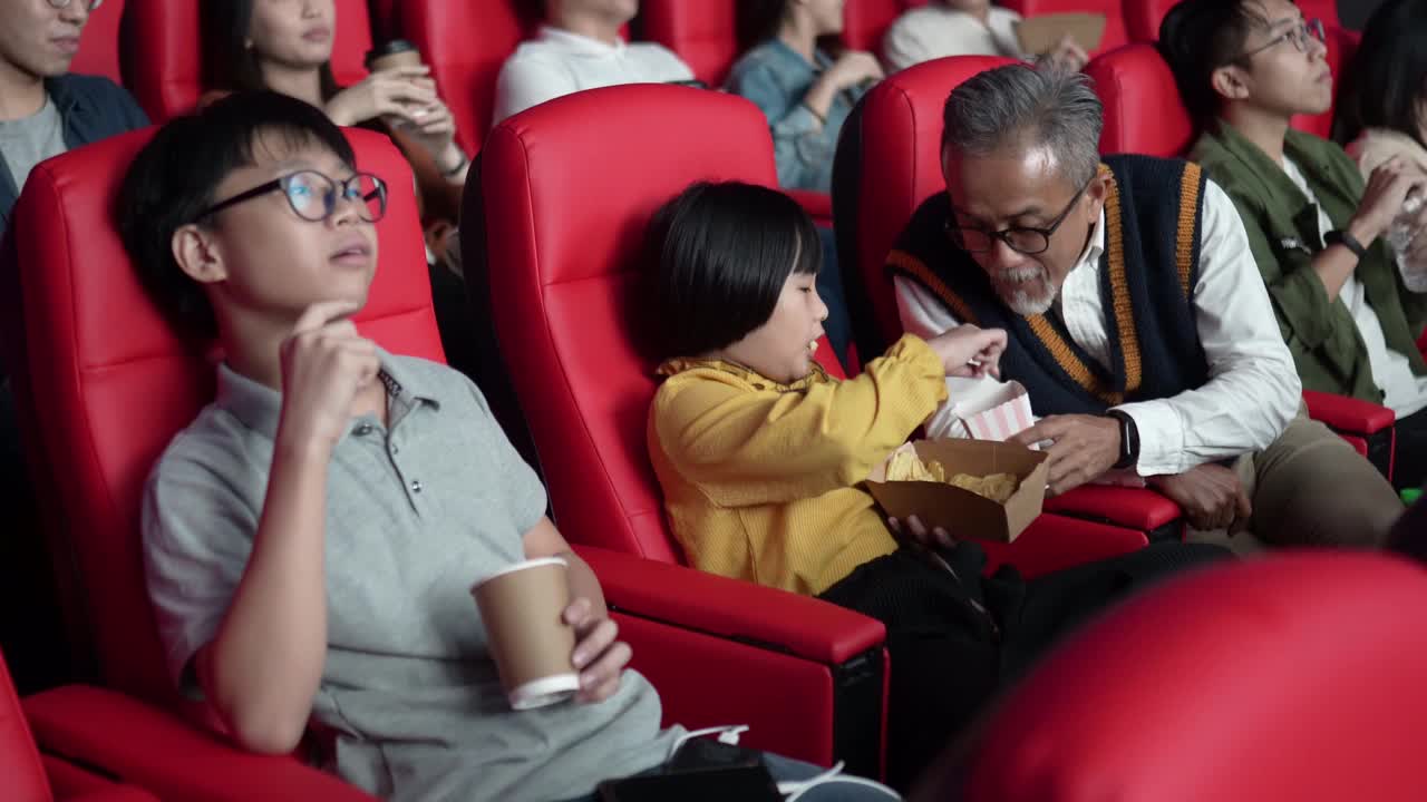 一位亚洲华人爷爷和他的孙子们喜欢在电影院看电影。