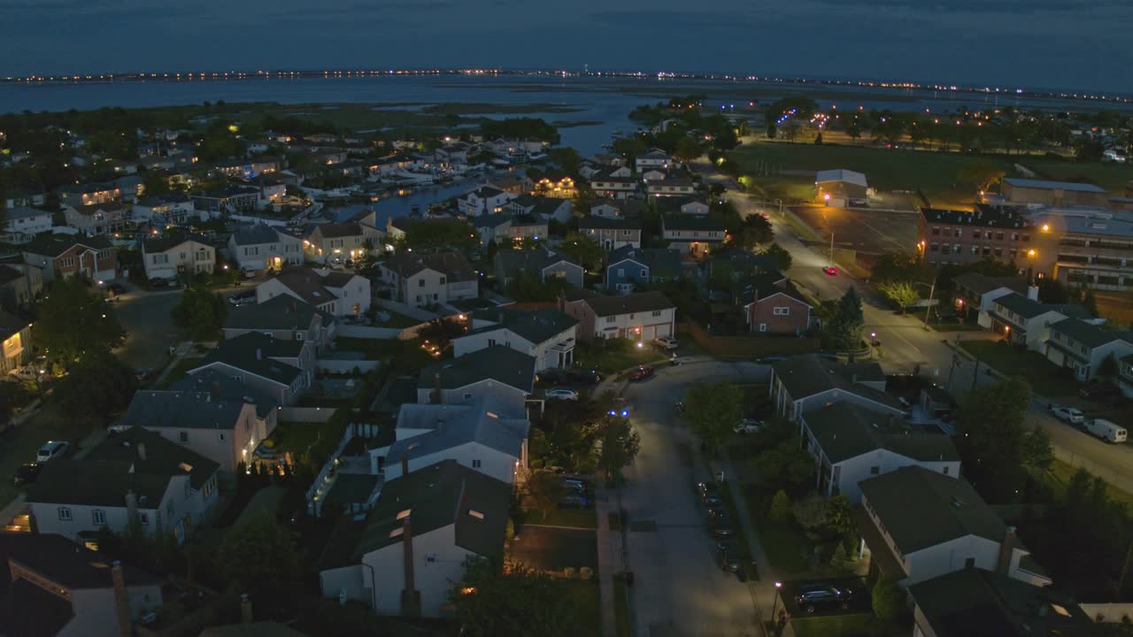 日落之后的夜晚，纽约皇后区欧辛赛德。航道周围的住宅区，私人船只停泊在码头上，由住宅和街灯照明。航拍视频，摄像机向前移动。