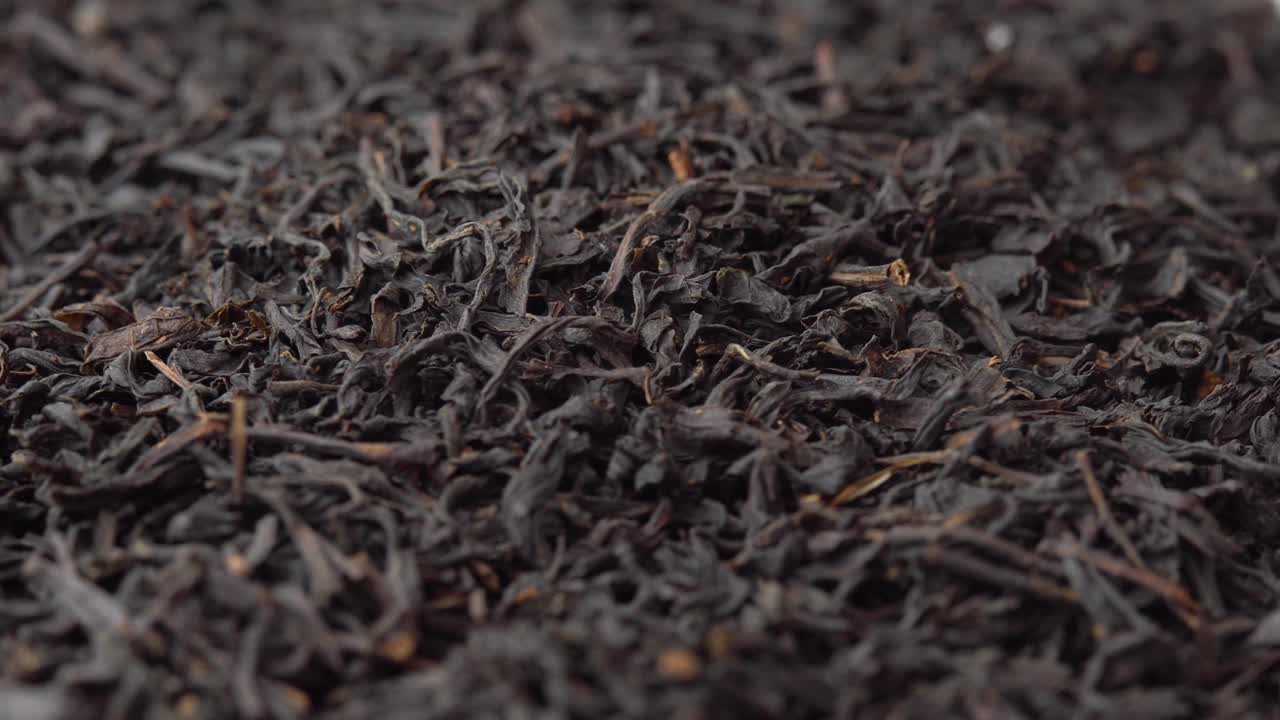 黑色散叶茶叶洒在盘子上并旋转特写，背景为咖啡馆或餐厅的茶叶广告