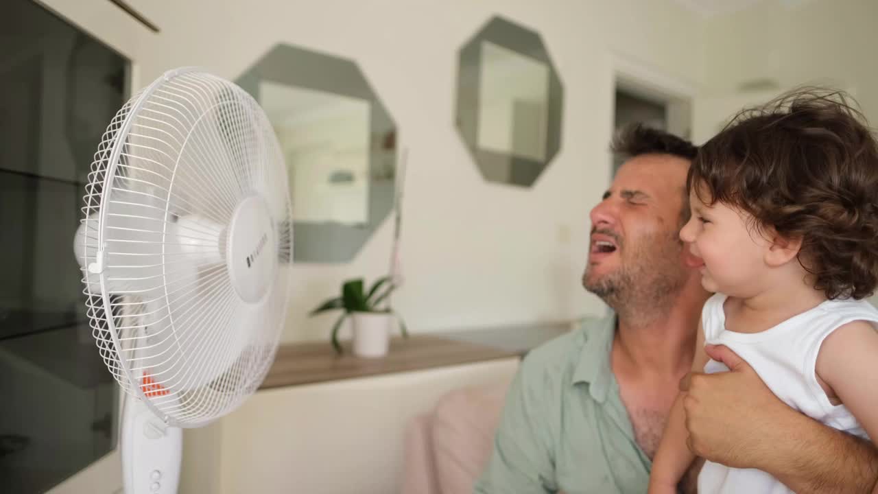 父亲孩子在炎热的夏天对着电风扇