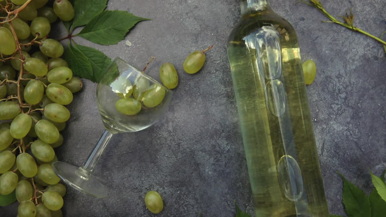 顶视图的瓶白葡萄酒，绿色藤蔓，葡萄酒杯和成熟的葡萄在vintage深色石头背景。酒店、酒吧、酒厂或品酒概念