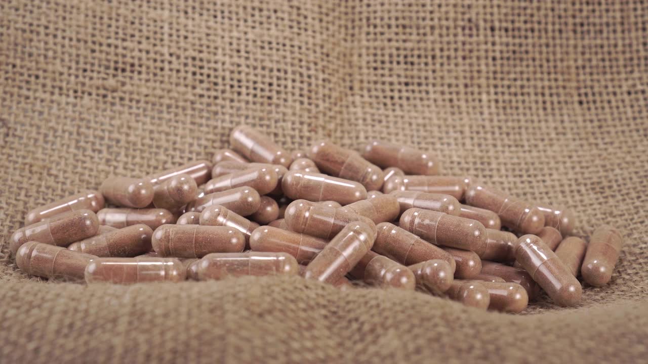 詳情圖-一只手在粗糙的粗麻袋上拿著藥用的棕色草藥膠囊