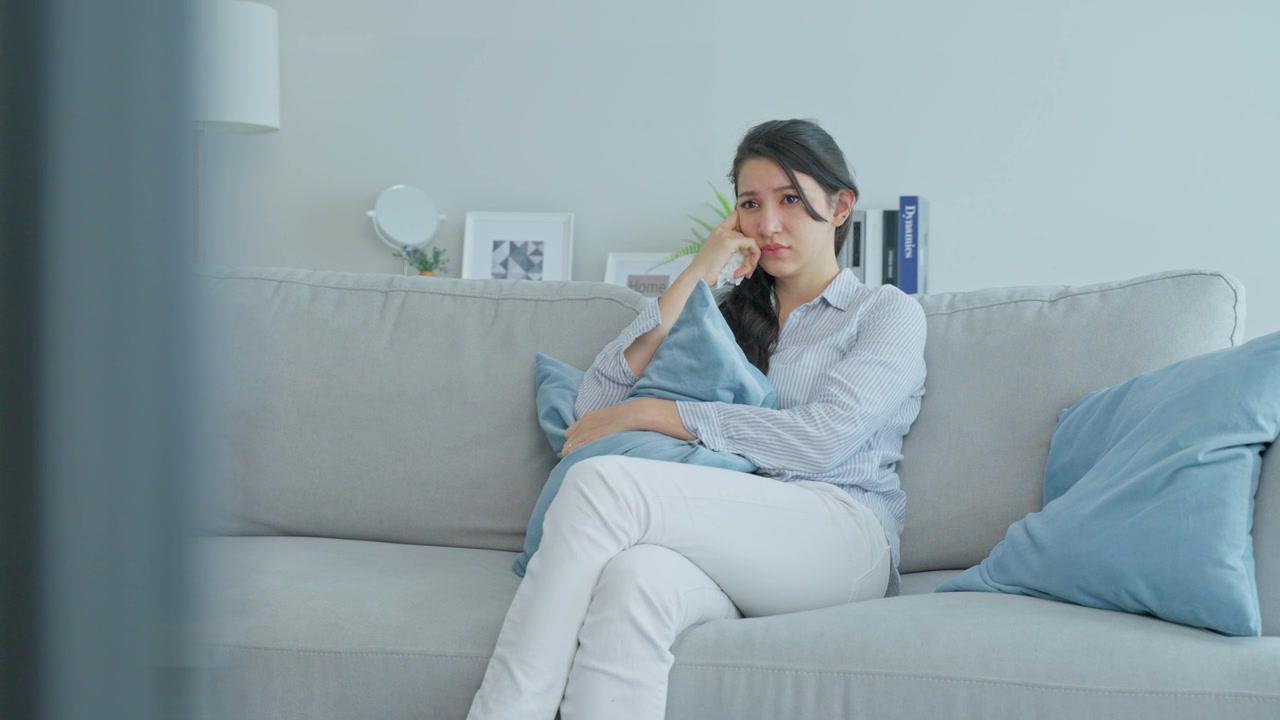 詳情圖-白人愛女人在客廳里看電視上的悲傷電影。漂亮的女性哭著哭著，坐在沙發(fā)上用遙控器看電視，在家里看電視上的戲劇和悲傷節(jié)目。