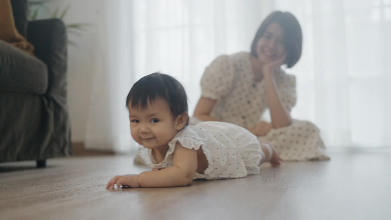 小女孩在房间的地板上爬着和年轻的妈妈