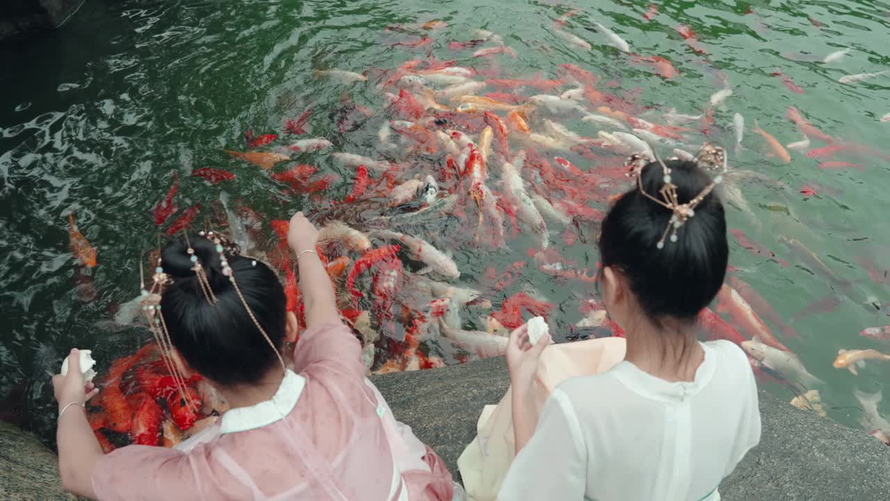 女孩们穿着汉服，在公园喂锦鲤。