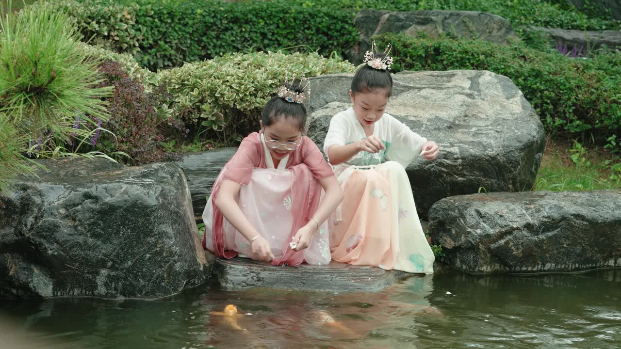 女孩们穿着汉服，在公园喂锦鲤。