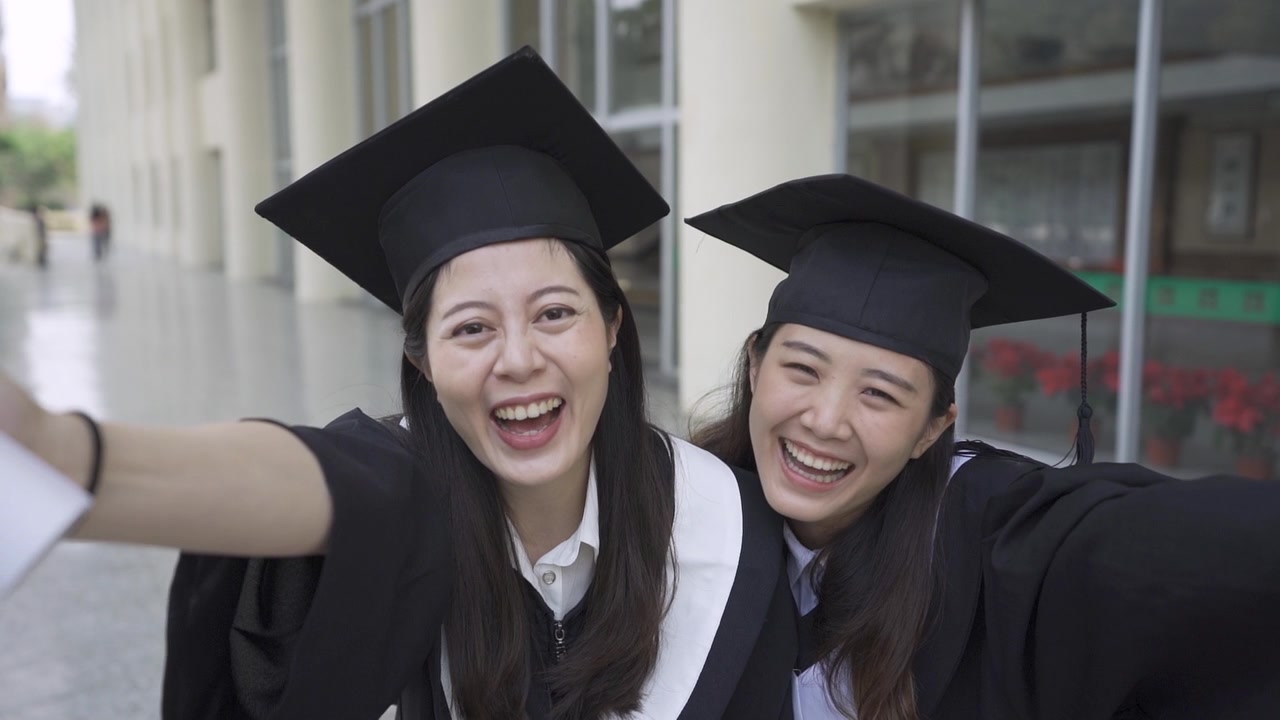 详情图-两个亚洲女大学生最好的朋友拥抱在一起，站在户外的草地上，面对镜头竖起大拇指，展示毕业典礼的毕业证书