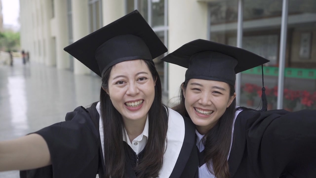 详情图-两个亚洲女大学生最好的朋友拥抱在一起，站在户外的草地上，面对镜头竖起大拇指，展示毕业典礼的毕业证书