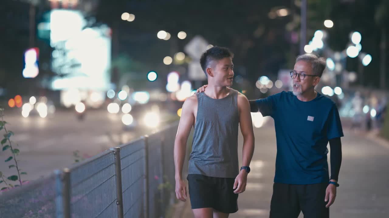 亚洲华人活跃的老人和他的儿子在晚上一起跑步锻炼后散步聊天城市