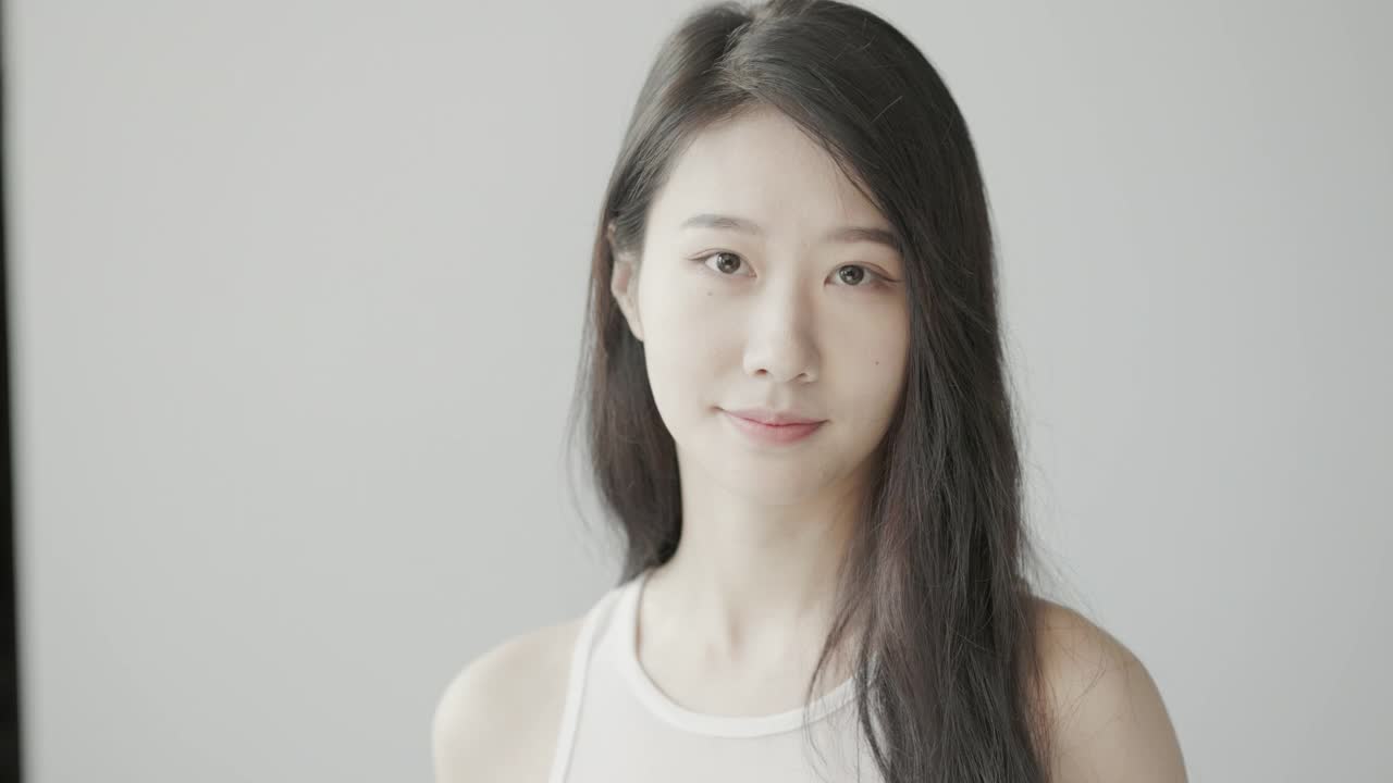 美丽的年轻亚洲女人与长长的黑色头发，看着镜子和拍摄慢动作在一个明亮的房间