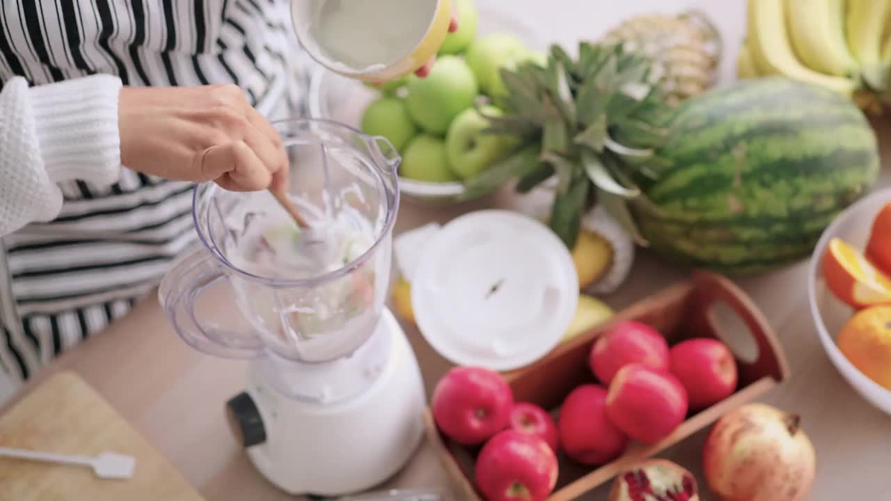 准备自制草莓，苹果奶昔，加入酸奶切水果搅拌机资深妇女手，高角度