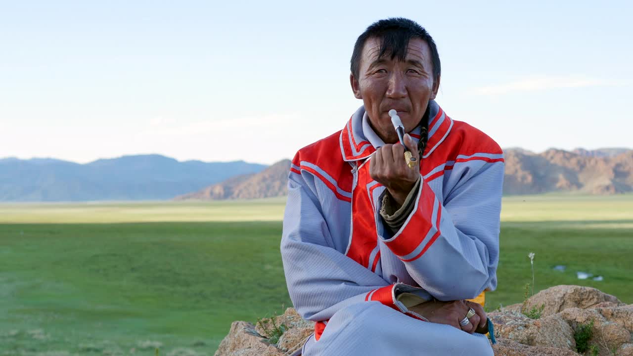 身着传统服饰的蒙古族牧民在西部阿尔泰山附近抽烟。